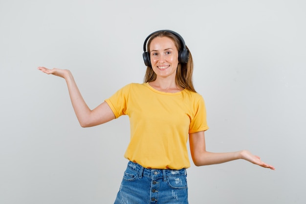 Jonge vrouw in t-shirt, korte broek, koptelefoon die handen opheft om evenwicht te tonen en er blij uitziet