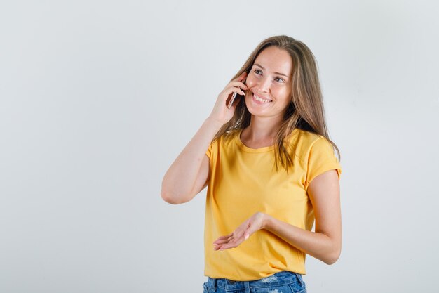 Jonge vrouw in t-shirt, korte broek praten over smartphone en op zoek vrolijk