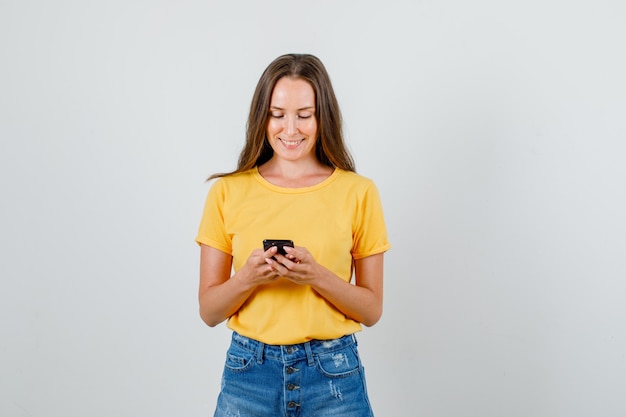 Jonge vrouw in t-shirt, korte broek smartphone kijken en glimlachen