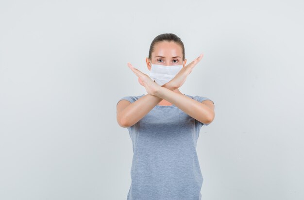 Jonge vrouw in t-shirt, masker dat stopgebaar toont en ernstig, vooraanzicht kijkt.