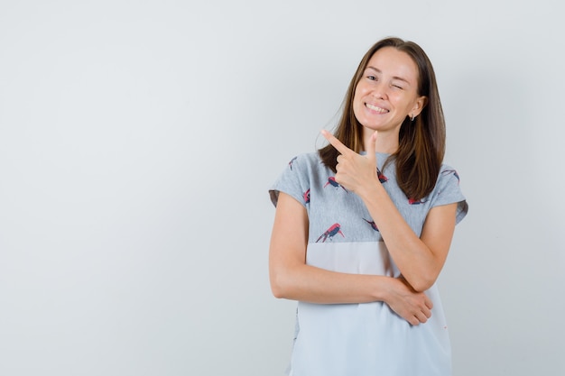 Jonge vrouw in t-shirt met pistoolgebaar en knipogend oog, vooraanzicht.