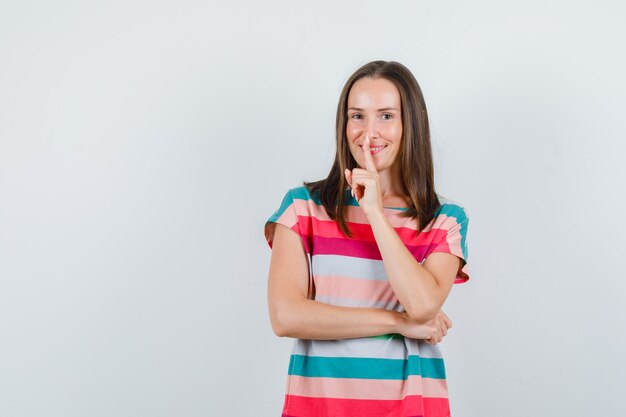 Jonge vrouw in t-shirt met stilte gebaar, vooraanzicht.