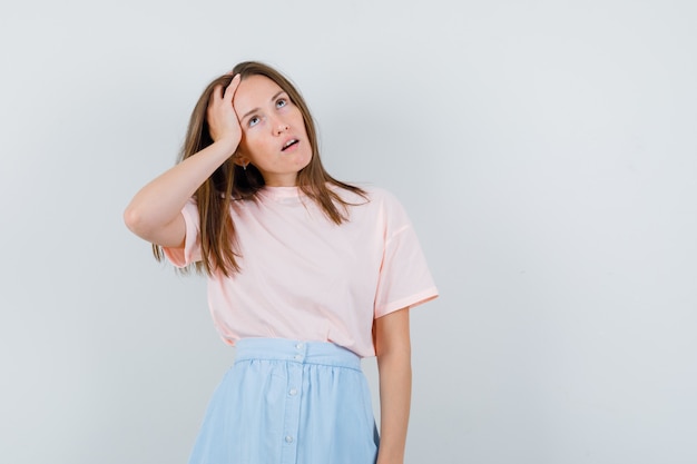 Jonge vrouw in t-shirt, rok die omhoog kijkt en peinzend, vooraanzicht kijkt.