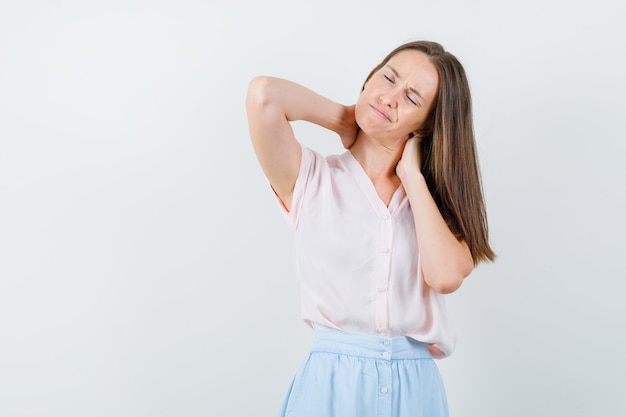 Jonge vrouw in t-shirt, rok hand in hand op nek en op zoek moe, vooraanzicht.