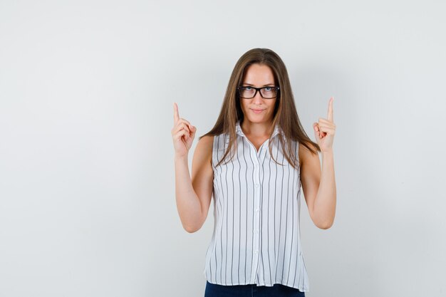 Jonge vrouw in t-shirt, spijkerbroek vingers omhoog, vooraanzicht.