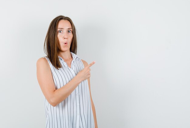 Jonge vrouw in t-shirt wijst naar kant en kijkt nieuwsgierig, vooraanzicht.