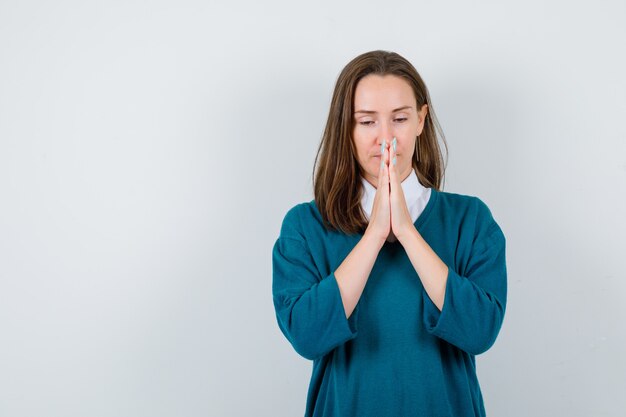 Jonge vrouw in trui over shirt met gevouwen handen in smekend gebaar en hoopvol, vooraanzicht.