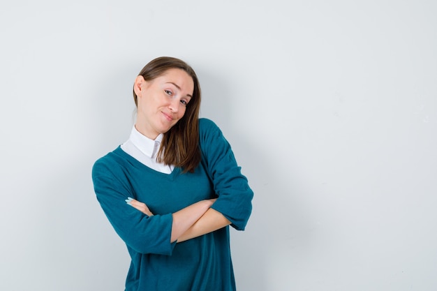 Jonge vrouw in trui over wit overhemd poseren met gevouwen armen en zelfverzekerd, vooraanzicht.