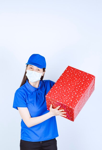Jonge vrouw in uniform en medisch masker met kerstcadeau.