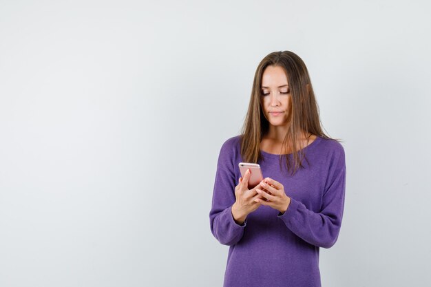 Jonge vrouw in violet overhemd met behulp van mobiele telefoon en op zoek naar druk, vooraanzicht.