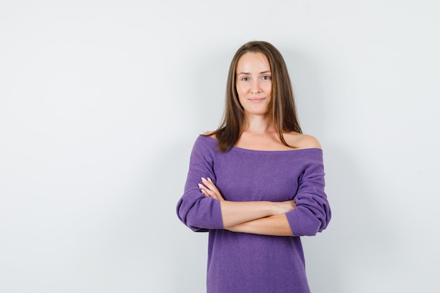 Jonge vrouw in violet overhemd staan met gekruiste armen en glimlachen, vooraanzicht.