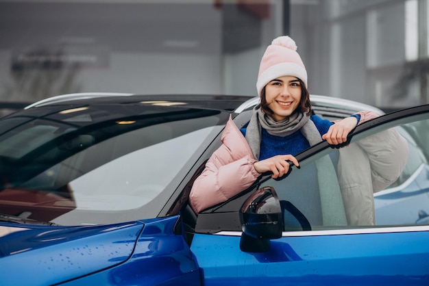 Jonge vrouw in winterjas blij met haar nieuwe blauwe auto