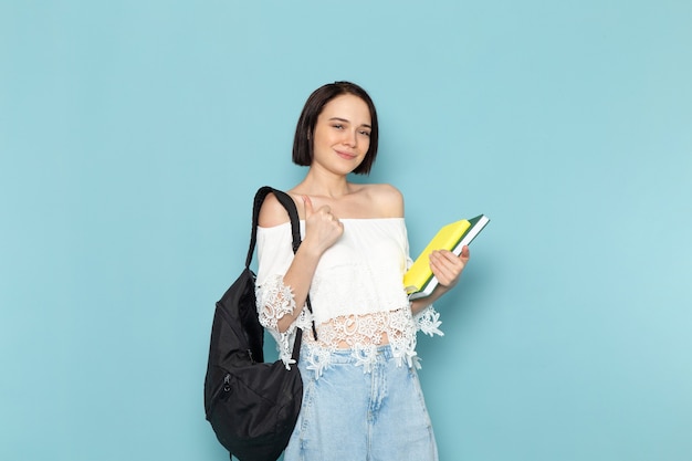 jonge vrouw in wit overhemd, blauwe spijkerbroek en zwarte tas met copybooks op blauw