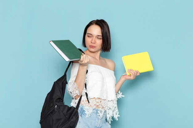 jonge vrouw in wit overhemd, blauwe spijkerbroek en zwarte tas met copybooks op blauw