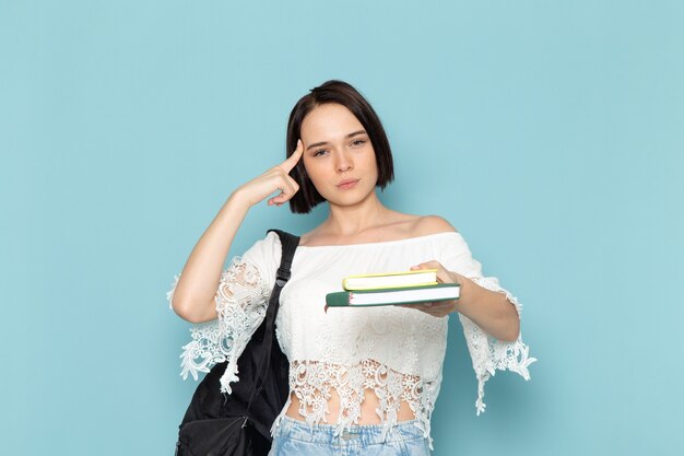 jonge vrouw in wit overhemd, blauwe spijkerbroek en zwarte tas met voorbeeldenboeken denken op blauw