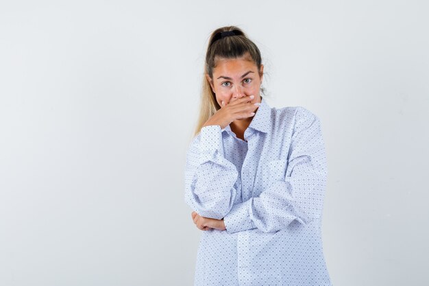 Jonge vrouw in wit overhemd dat mond behandelt met hand, gelukkig glimlacht kijkt