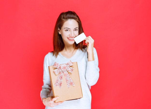 Jonge vrouw in wit overhemd die een kartonnen geschenkdoos vasthoudt en haar visitekaartje presenteert