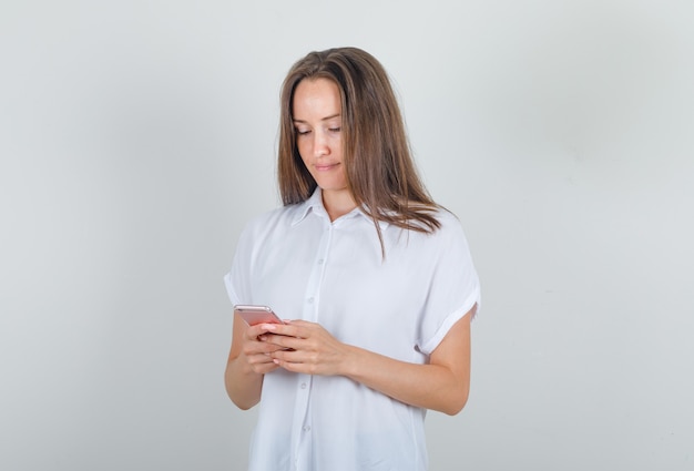 Jonge vrouw in wit t-shirt met behulp van smartphone en bezig op zoek