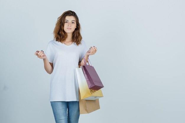 Jonge vrouw in wit t-shirt, spijkerbroek met papieren zakken en op zoek charmant, vooraanzicht.