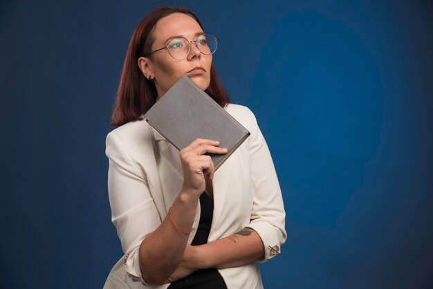 Jonge vrouw in witte blazer die een boek houdt en denkt.