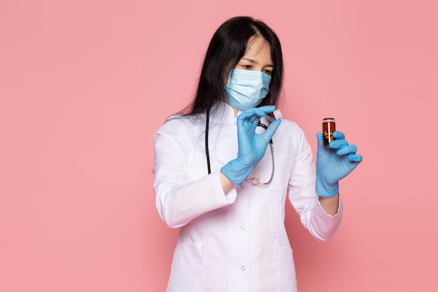 jonge vrouw in witte medische pak blauwe handschoenen blauw beschermend masker kan met pillen op roze