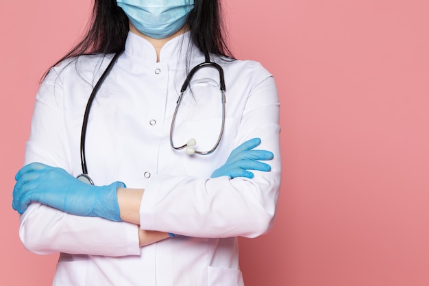 Jonge vrouw in witte medische pak blauwe handschoenen blauw beschermend masker met stethoscoop op roze