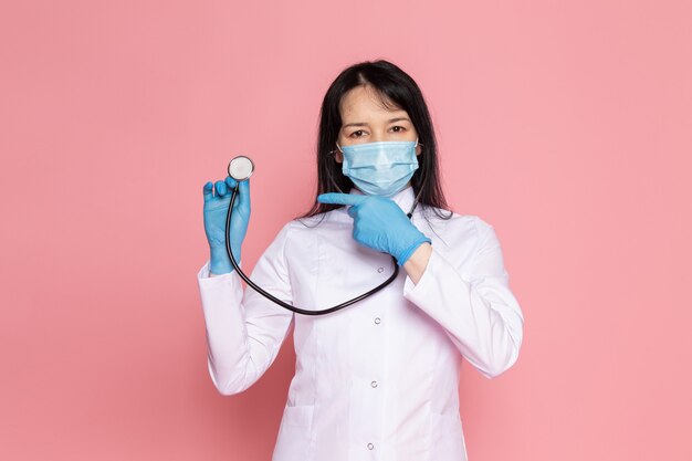 jonge vrouw in witte medische pak blauwe handschoenen blauw beschermend masker met stethoscoop op roze