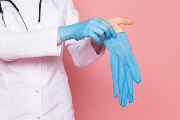 jonge vrouw in witte medische pak blauwe handschoenen blauw beschermend masker met stethoscoop op roze