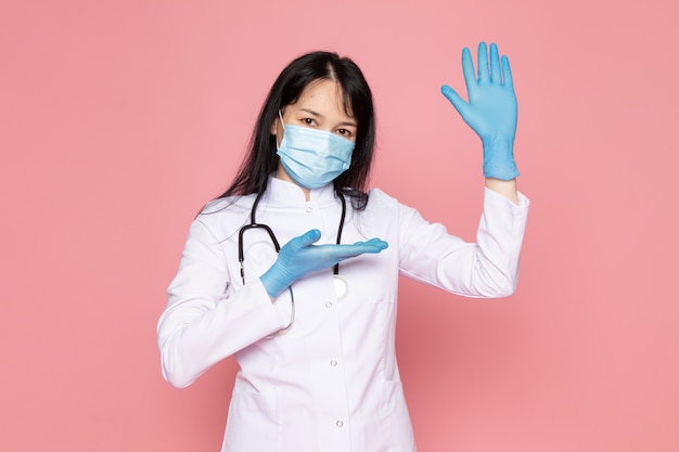 jonge vrouw in witte medische pak blauwe handschoenen blauw beschermend masker met stethoscoop op roze