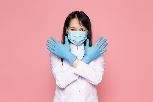 jonge vrouw in witte medische pak blauwe handschoenen blauw beschermend masker met stethoscoop op roze