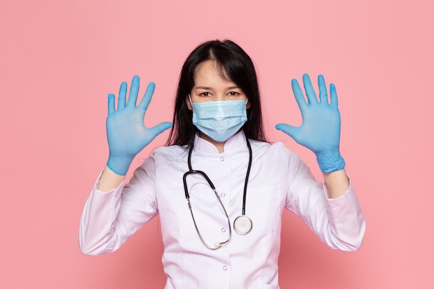 Jonge vrouw in witte medische pak blauwe handschoenen blauw beschermend masker met stethoscoop op roze