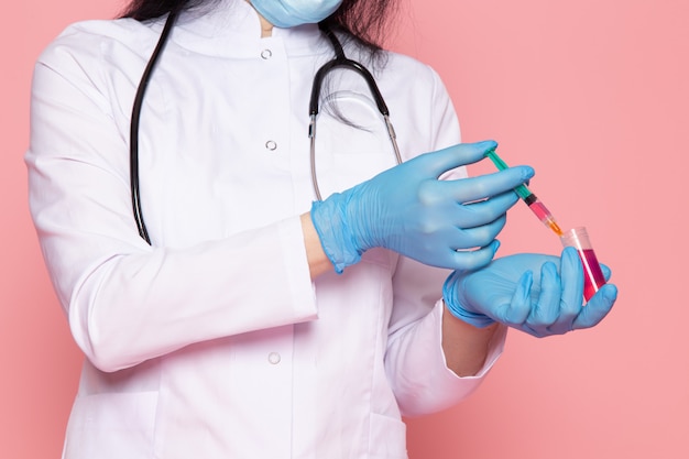 jonge vrouw in witte medische pak blauwe handschoenen blauw beschermend masker op roze