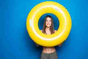 Gratis foto jonge vrouw in zomerslijtage met opblaasbare ring die over blauwe muur wordt geïsoleerd.