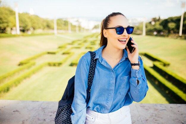 Jonge vrouw in zonnebril praten op een mobiele telefoon tegen de achtergrond van een plant