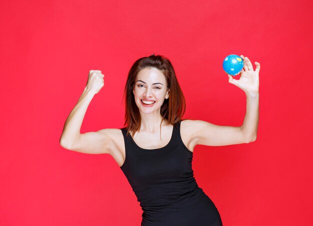 Jonge vrouw in zwart hemd die een mini-wereldbol vasthoudt en zich sterk voelt