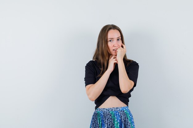 Jonge vrouw in zwart t-shirt en blauwe rok die wang aan kant leunen en aan iets denken en peinzend kijken