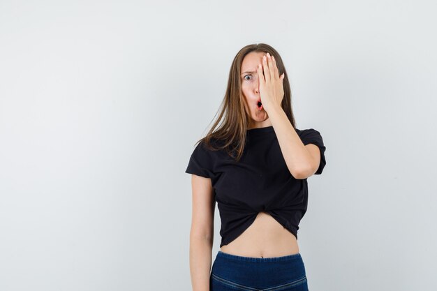 Jonge vrouw in zwarte blouse die haar hand op één oog bedekt en angstig kijkt