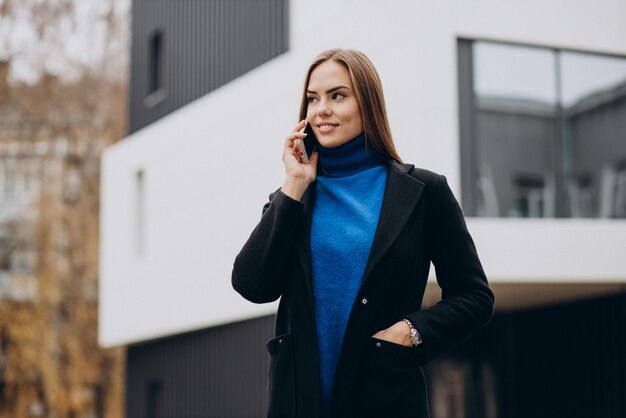 Jonge vrouw in zwarte jas die telefoon gebruikt