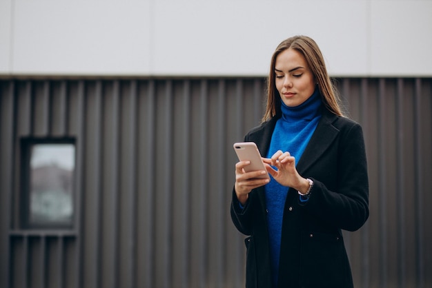 Jonge vrouw in zwarte jas die telefoon gebruikt