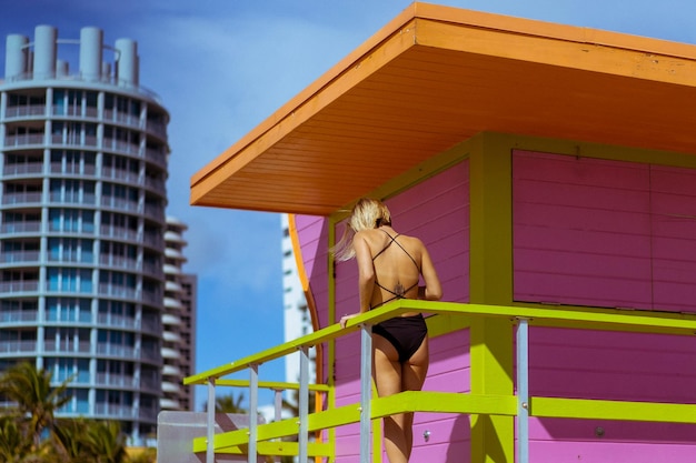 Gratis foto jonge vrouw in zwarte zwembroek op het strand miami florida usa in de buurt van de badmeestertoren.