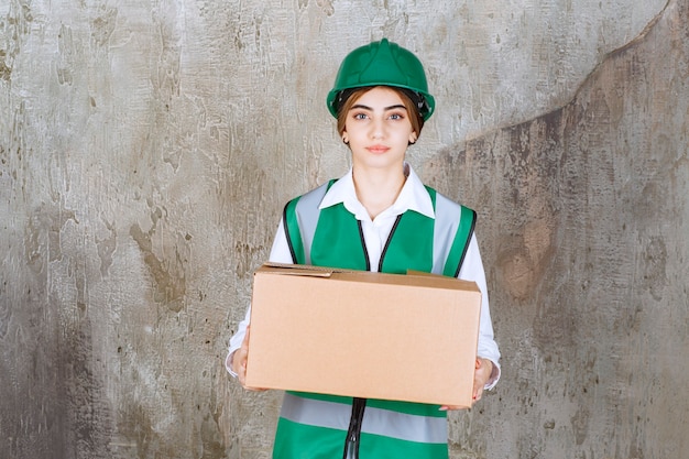 Jonge vrouw ingenieur in groen vest en helm met papieren doos