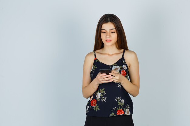 Jonge vrouw kijkt naar smartphone in blouse en ziet er druk uit, vooraanzicht.