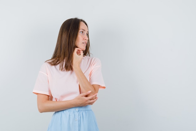 Jonge vrouw kijkt opzij in t-shirt, rok en kijkt gericht, vooraanzicht.