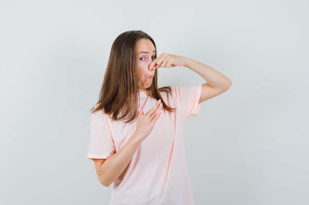 Jonge vrouw knijpen neus als gevolg van slechte geur in roze t-shirt en walgt, vooraanzicht.