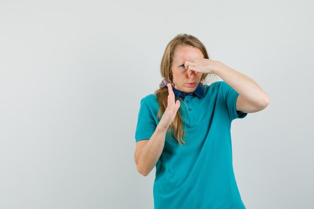 Jonge vrouw knijpen neus als gevolg van slechte geur in t-shirt en walgt op zoek.