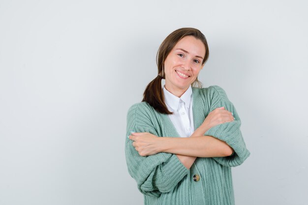 Jonge vrouw knuffelt zichzelf in blouse, vest en ziet er gelukkig uit, vooraanzicht.