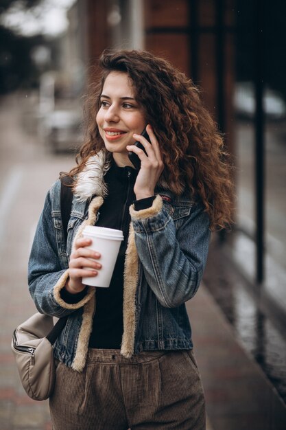 Jonge vrouw koffie drinken en het gebruik van de telefoon