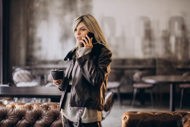 Jonge vrouw koffie drinken en praten aan de telefoon in een café