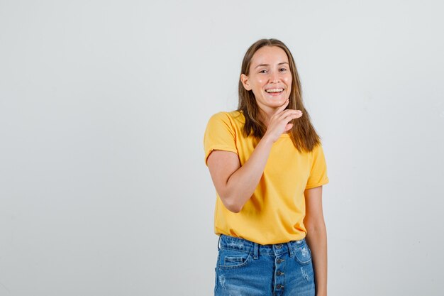 Jonge vrouw lachen met vinger op kin in t-shirt, korte broek