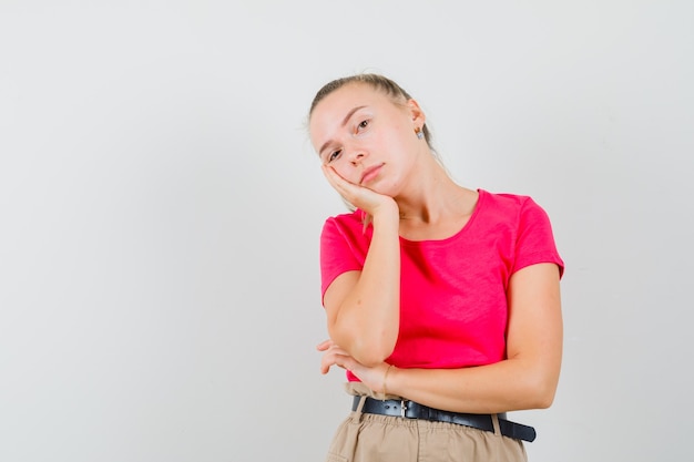 Jonge vrouw leunend wang op opgeheven palm in t-shirt en broek en peinzend op zoek